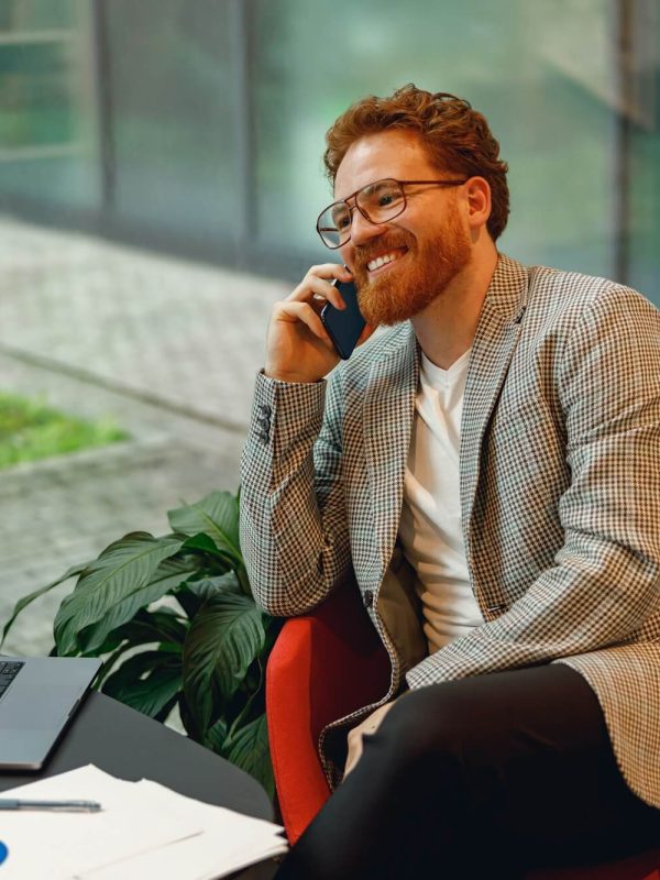 smiling-male-boss-talking-phone-with-client-while-sitting-in-coworking-space-and-working-on.jpg